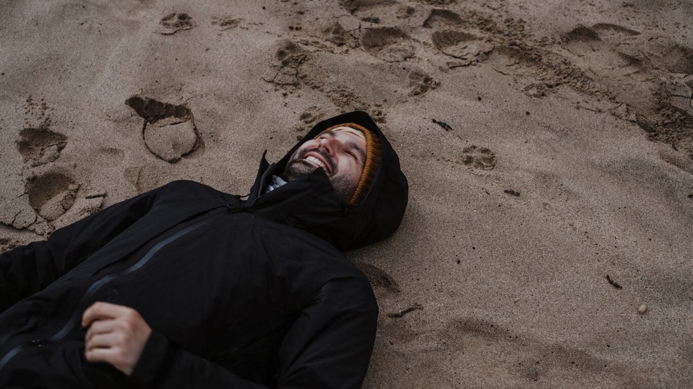 Smiling man in a black raincoat lying on a sand in Autumn